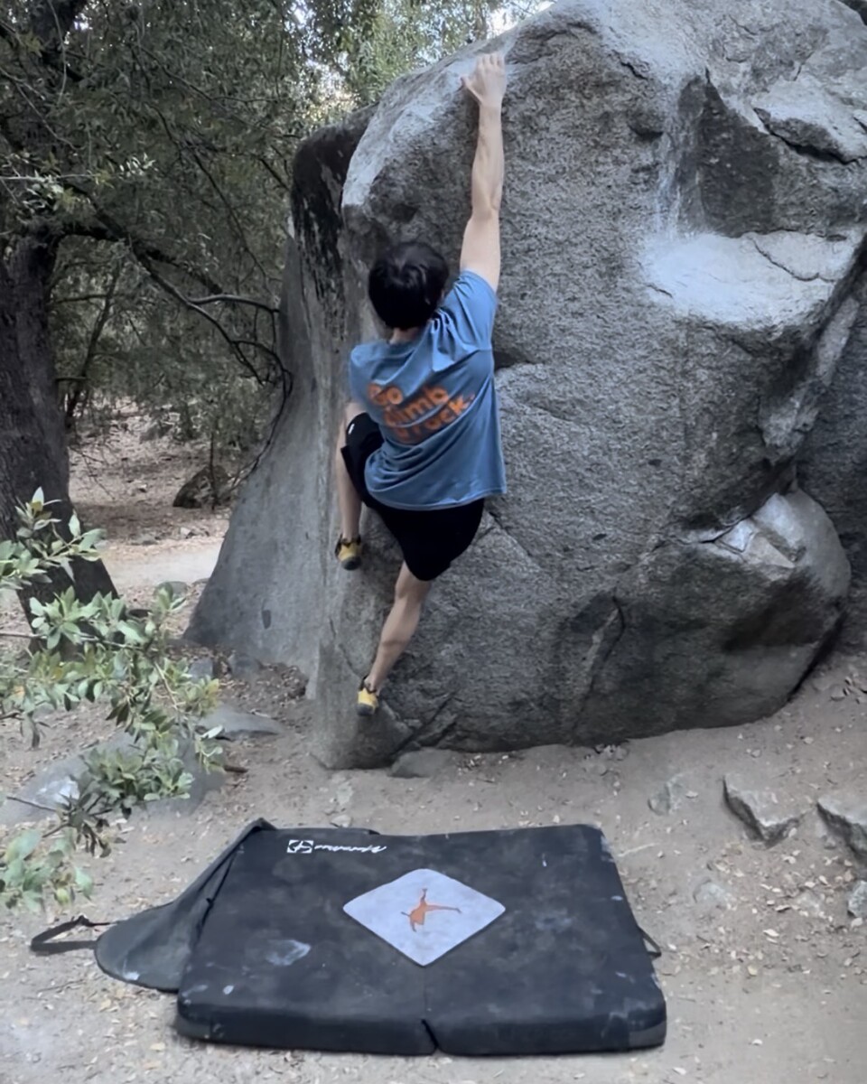Evan climbing a boulder above a crash pad